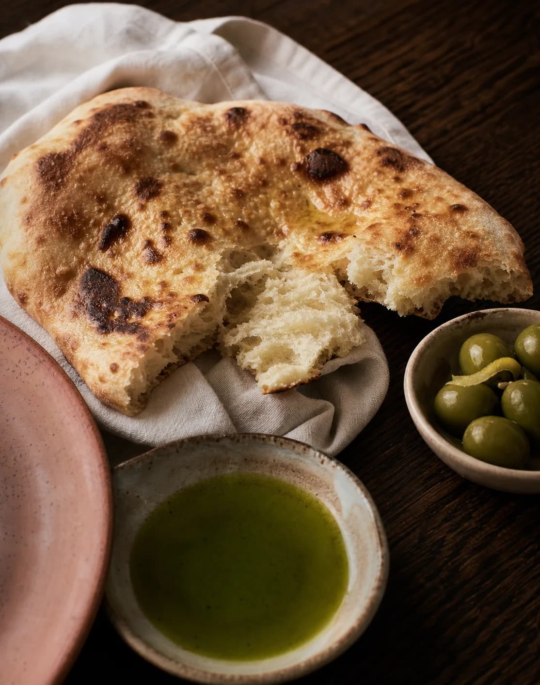 Warm flatbread with olive oil and green olives on cream linen